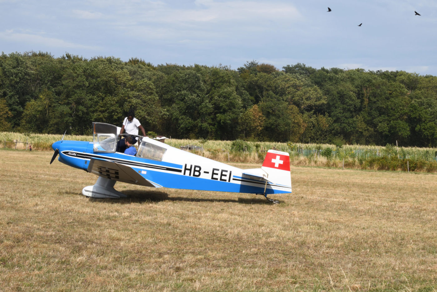 Photography taken during a show, in which we see a little plane with a person in it, and a person standing outside the plane.
