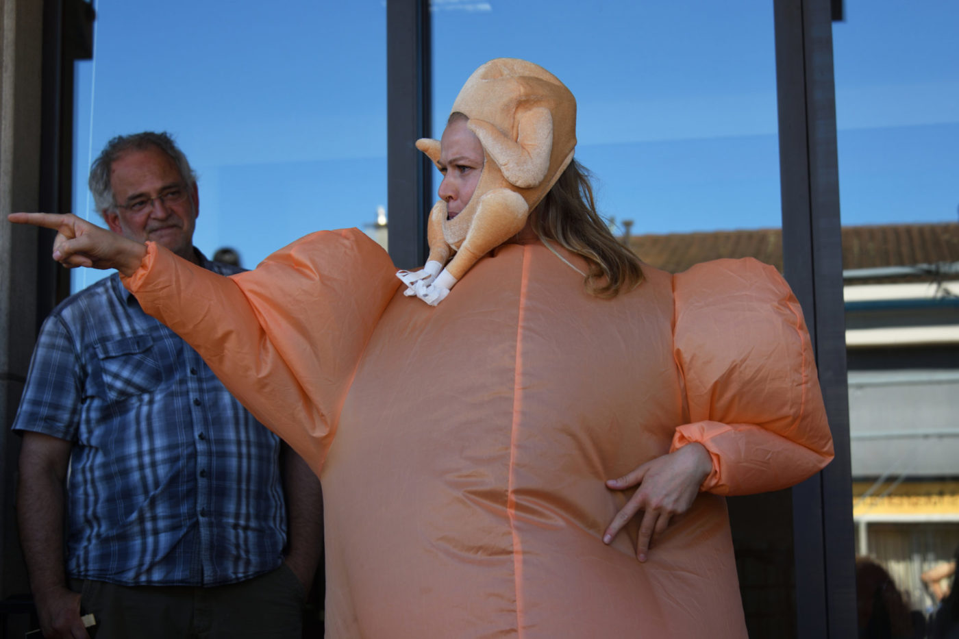 Danae Dario porte un déguisement orange gonflé. Elle a un poulet cuit artificiel autour de son visage. Elle se tient devant la porte vitrée d'une salle de spectacle, à l'extérieur.