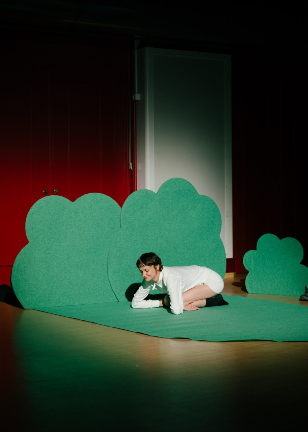 La comédienne Marion Thomas se tient comme un mouton, par terre, sur une moquette verte en forme de buisson.