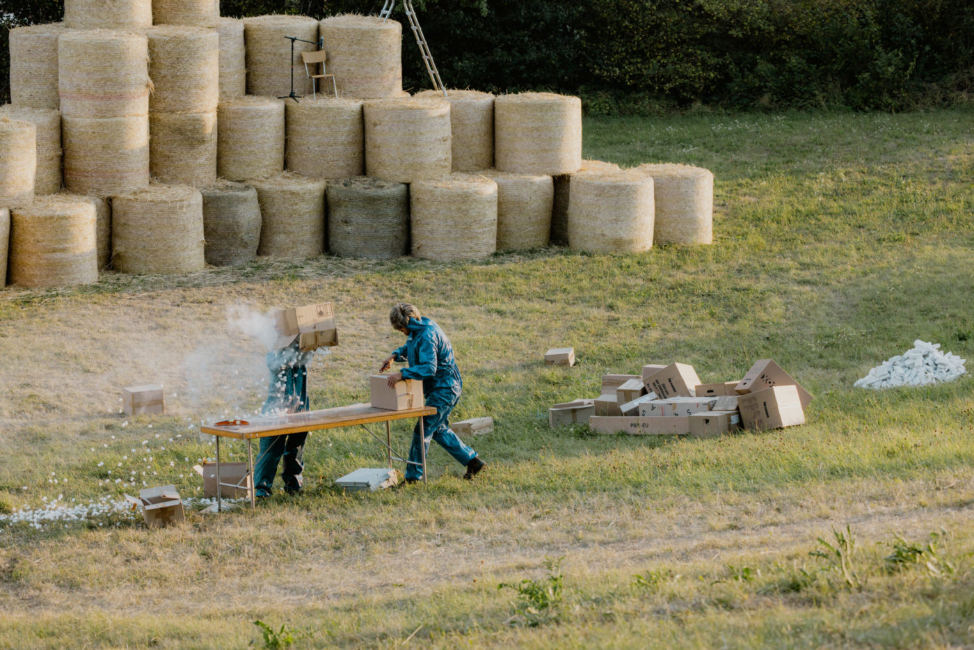 Deux personnes sont dans un champ, devant des bottes de foin. Le spectacle a lieu dans une parcelle agricole au Muids.